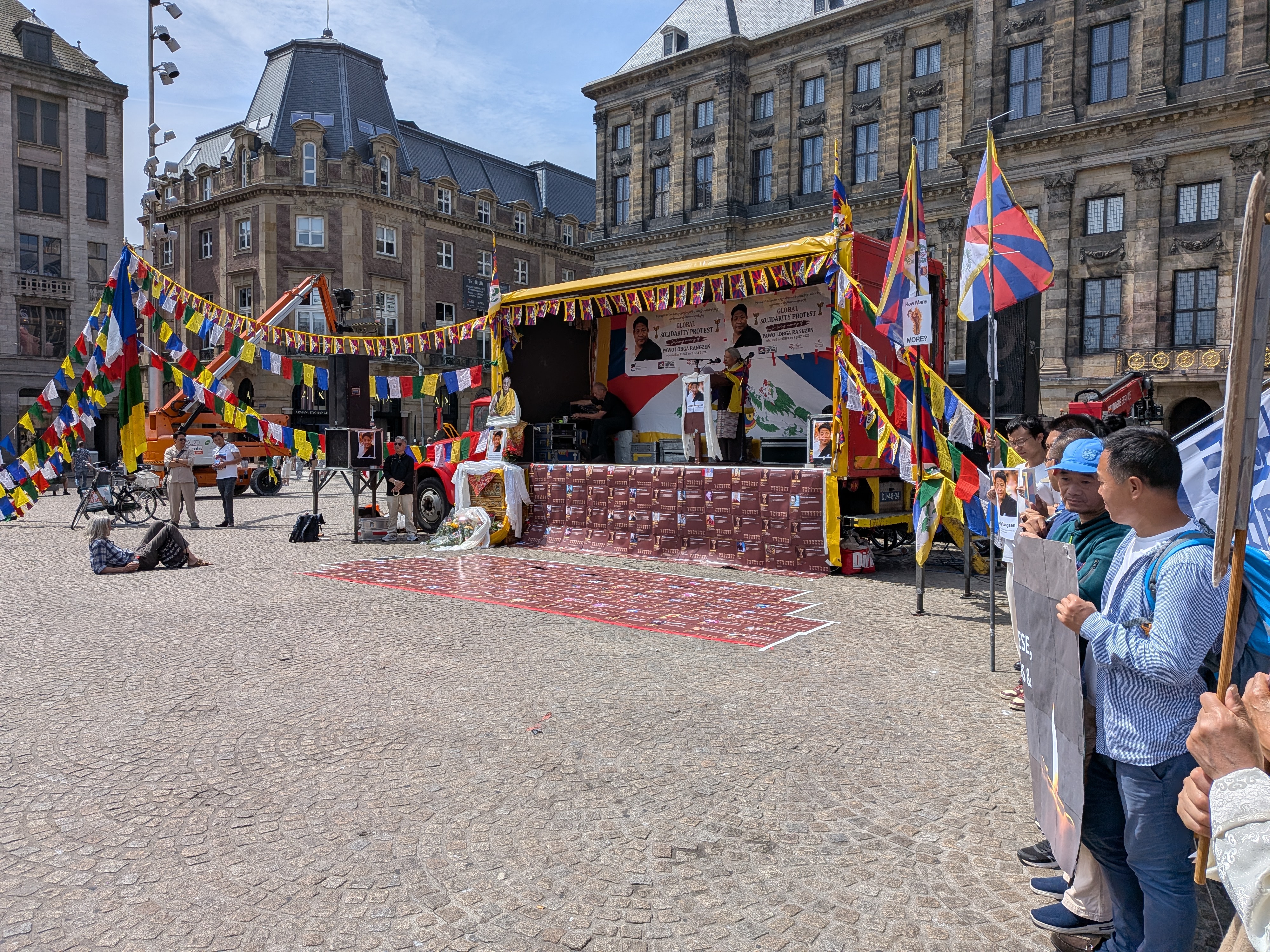Podium op de Dam met het spandoek Global Solidarity Protest voor Pawo Lobga Rangzen, Tibetaanse vlaggen en een gedenkplaats