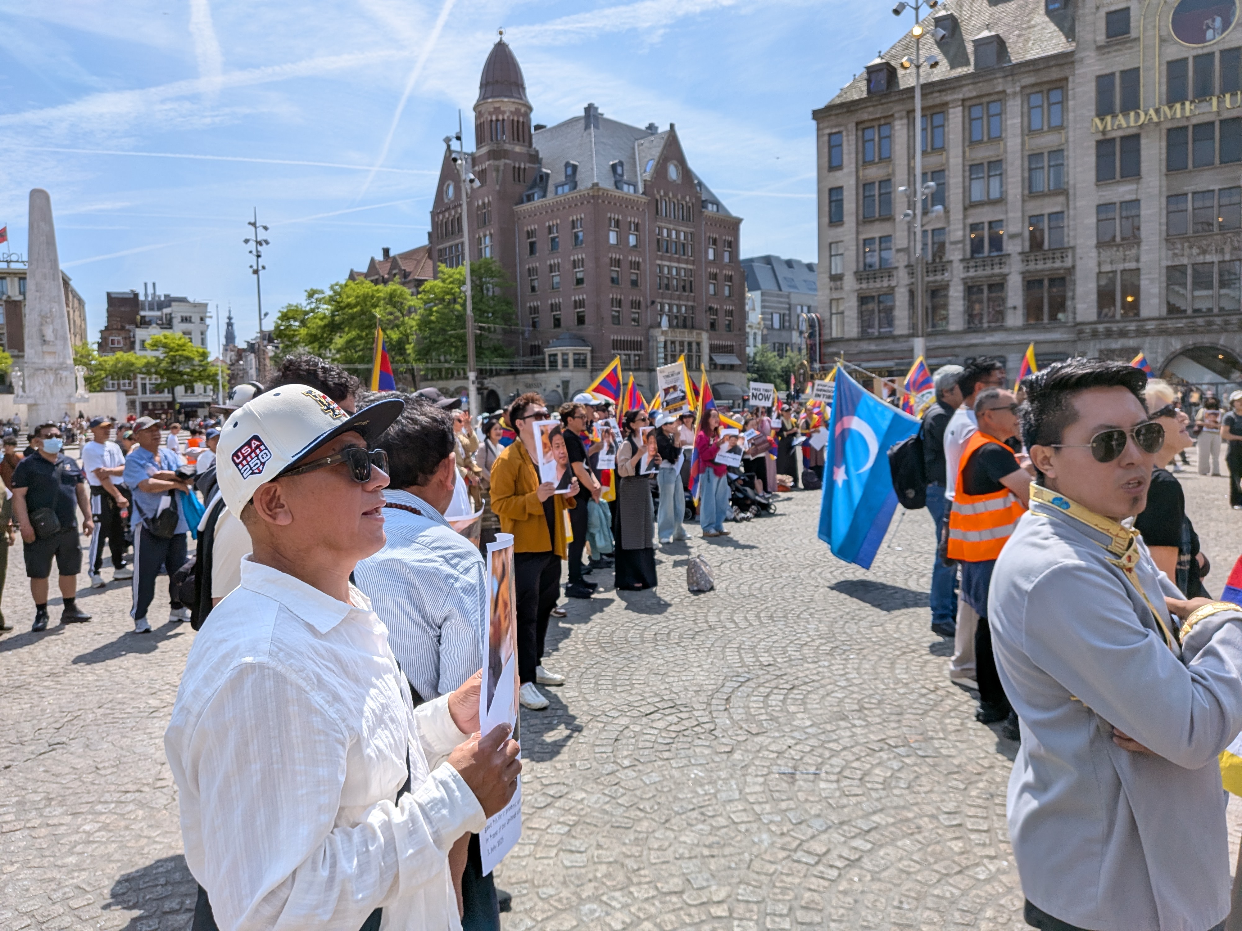 Grote menigte demonstranten op de Dam met Tibetaanse vlaggen en de vlag van Oost-Turkestan
