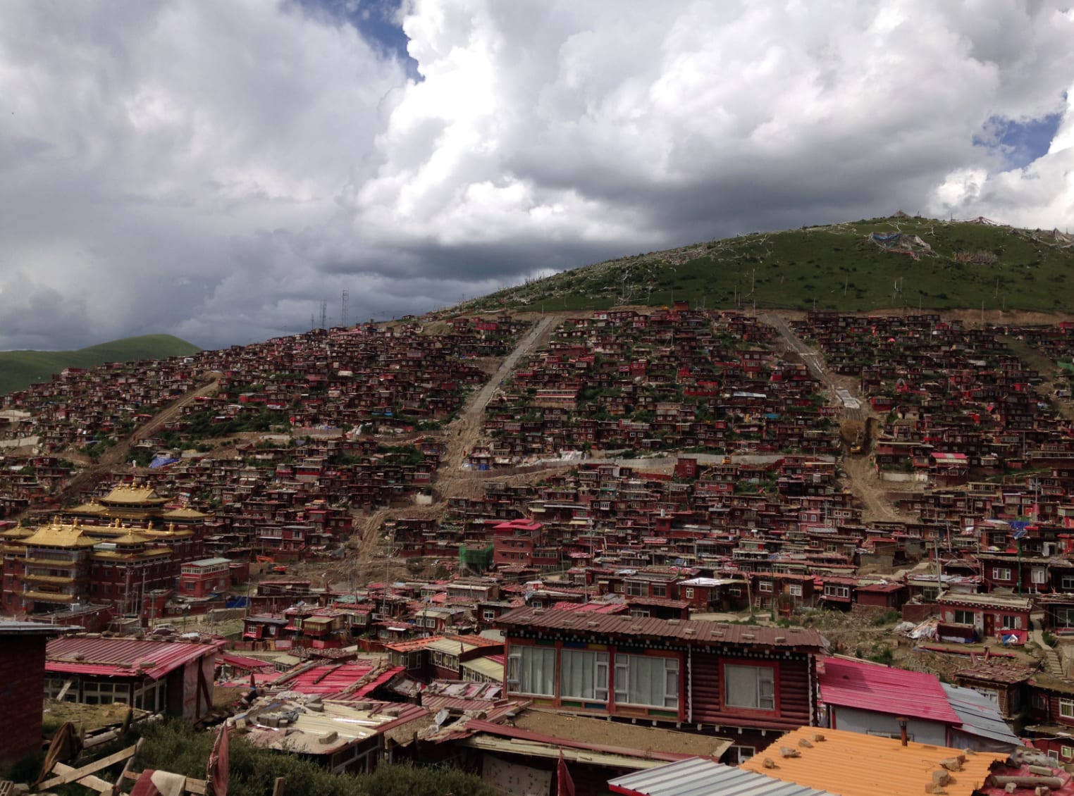 Larung Gar tegen de berghelling: duizenden rode woningen van monniken en nonnen, doorsneden door kale sloopsporen en bouwwegen